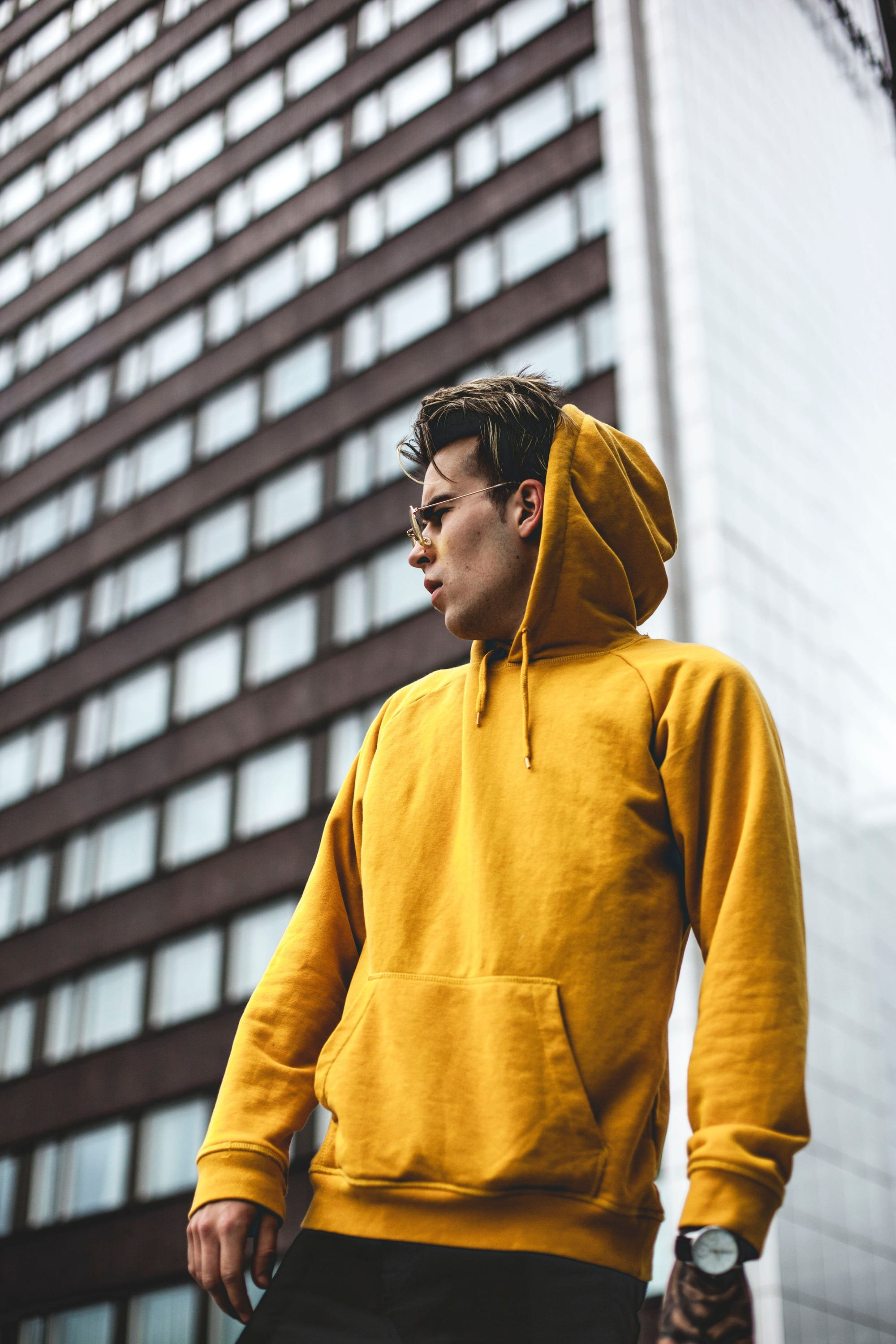 A man in a yellow hooded sweatshirt below a tall building