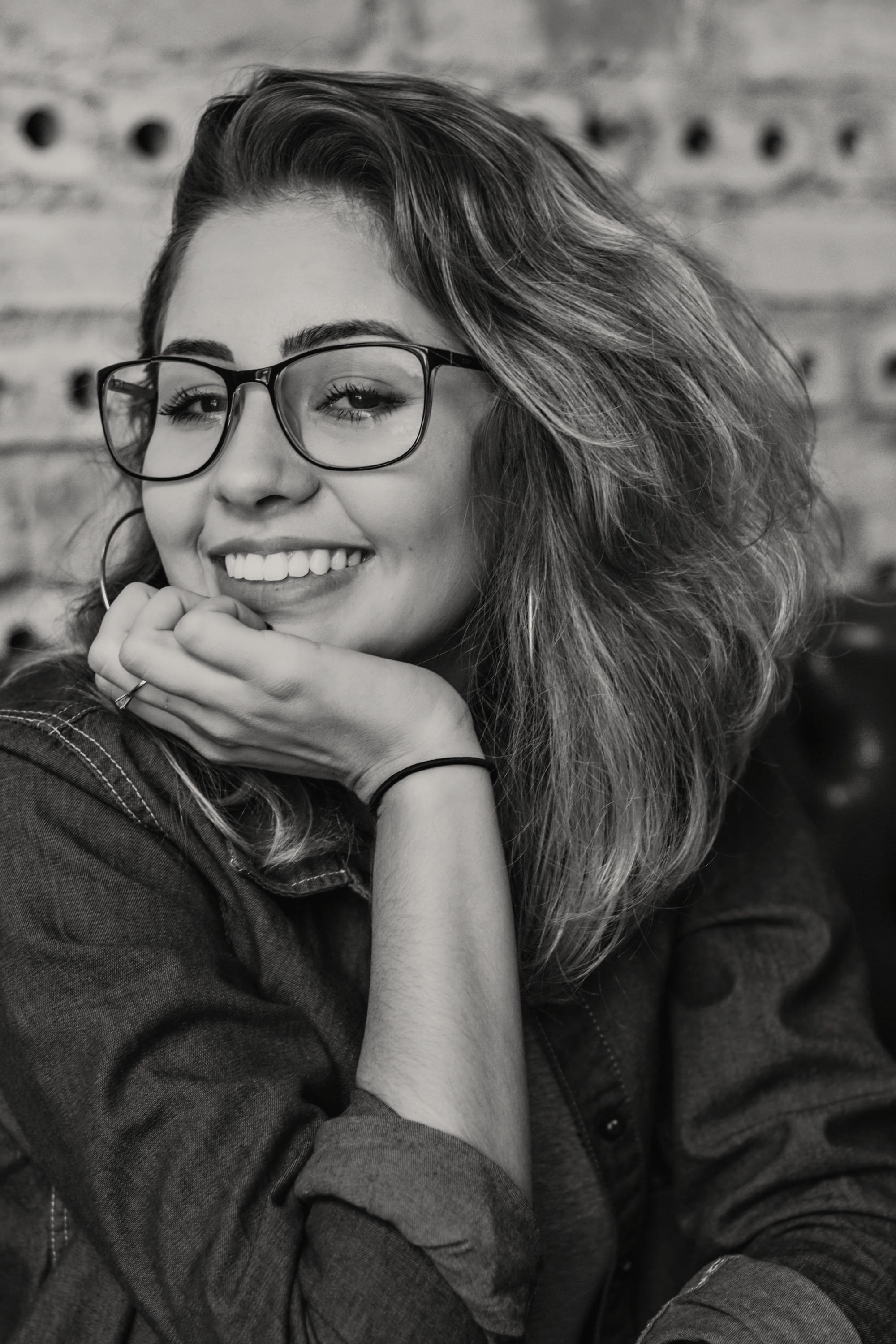 A woman in a denim shirt resting her chin on her hand, smiling