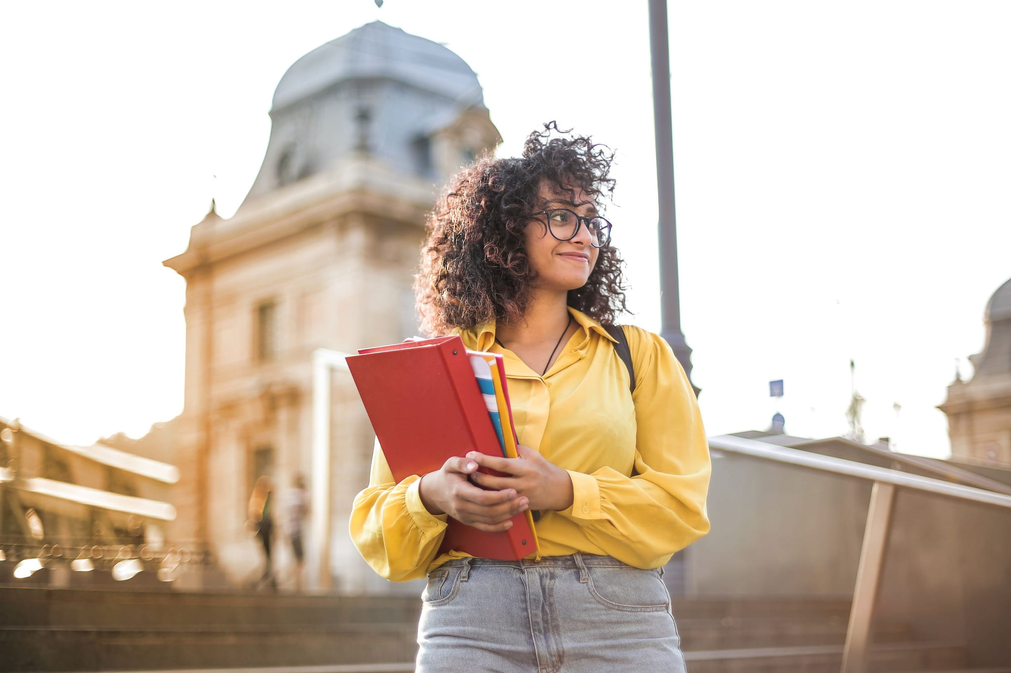 A student with a red notebook, laughing, in front of a domed building
